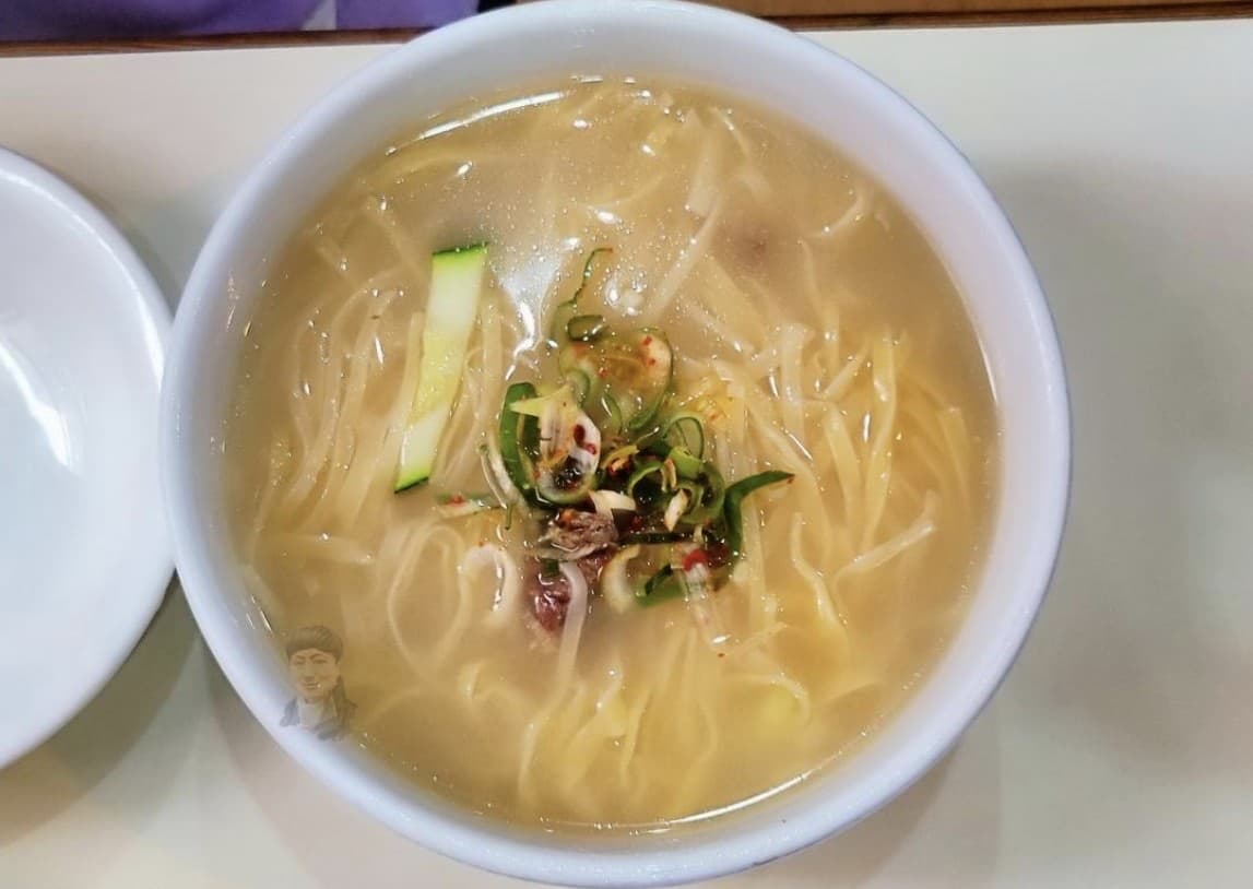 A bowl of Andong-style guksu — thin noodles in a light clear broth topped with zucchini strips and chili scallions