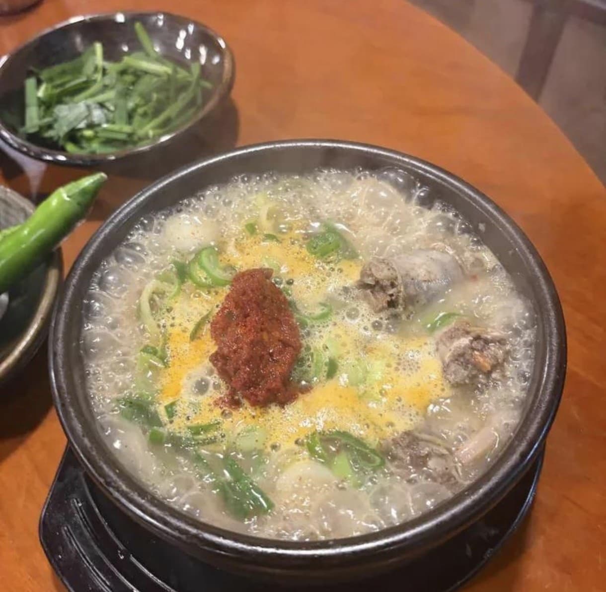 A stone pot of bubbling milky sundae gukbap soup topped with a scoop of red seasoning paste and scallions
