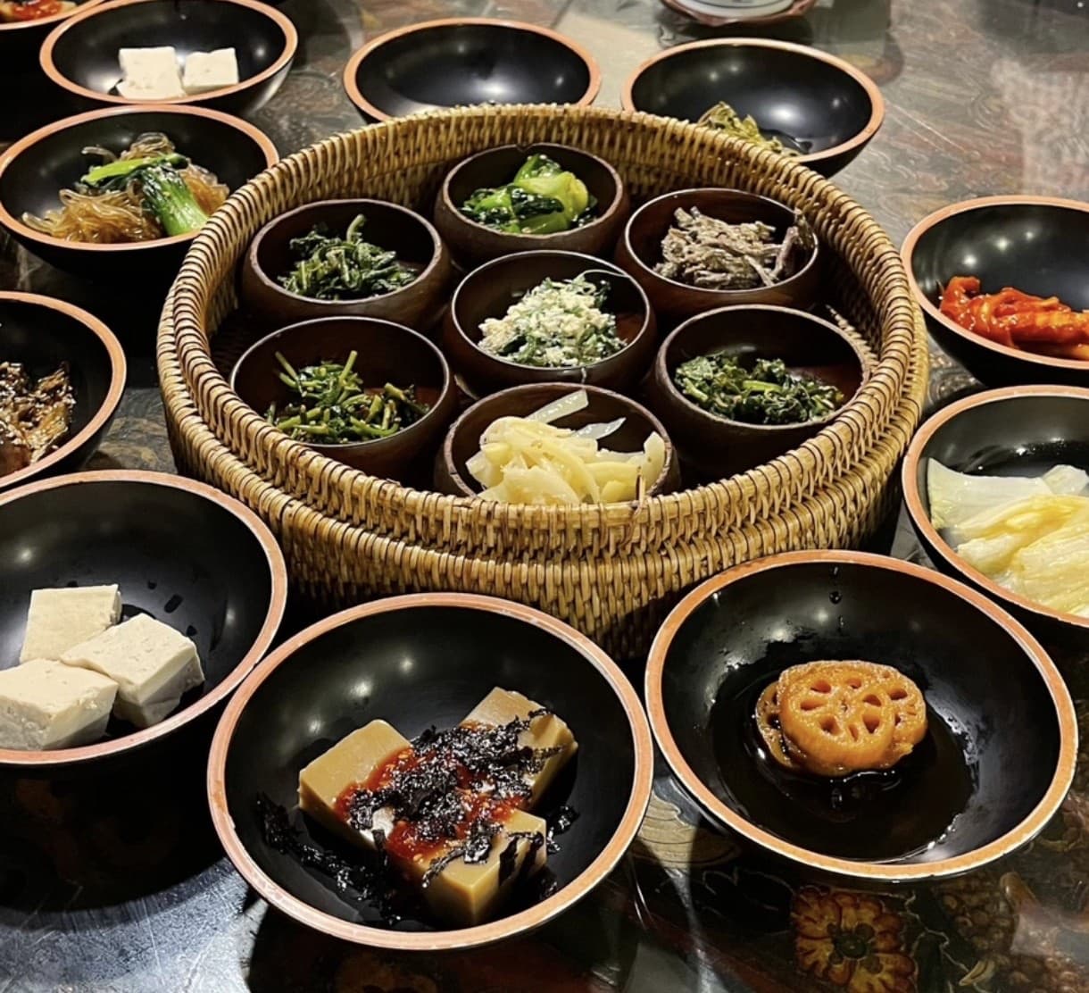 Sanchon temple cuisine — a wicker basket of small bowls of assorted seasoned wild greens, surrounded by more banchan side dishes