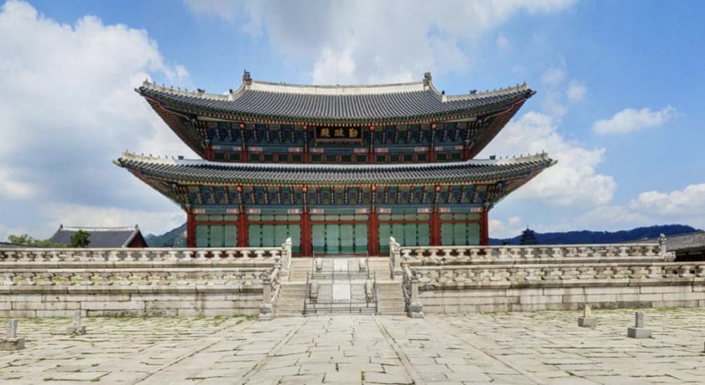 Geunjeongjeon throne hall seen across the empty stone courtyard of the palace under a blue sky
