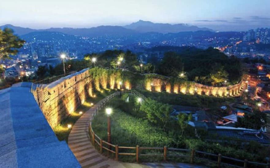 Illuminated Seoul City Wall winding along the Bukaksan ridge at twilight with the cityscape behind
