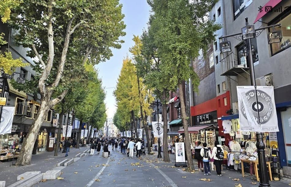 Tree-lined Insadong pedestrian street in autumn with yellow ginkgo trees, banners, shops, and crowds of visitors