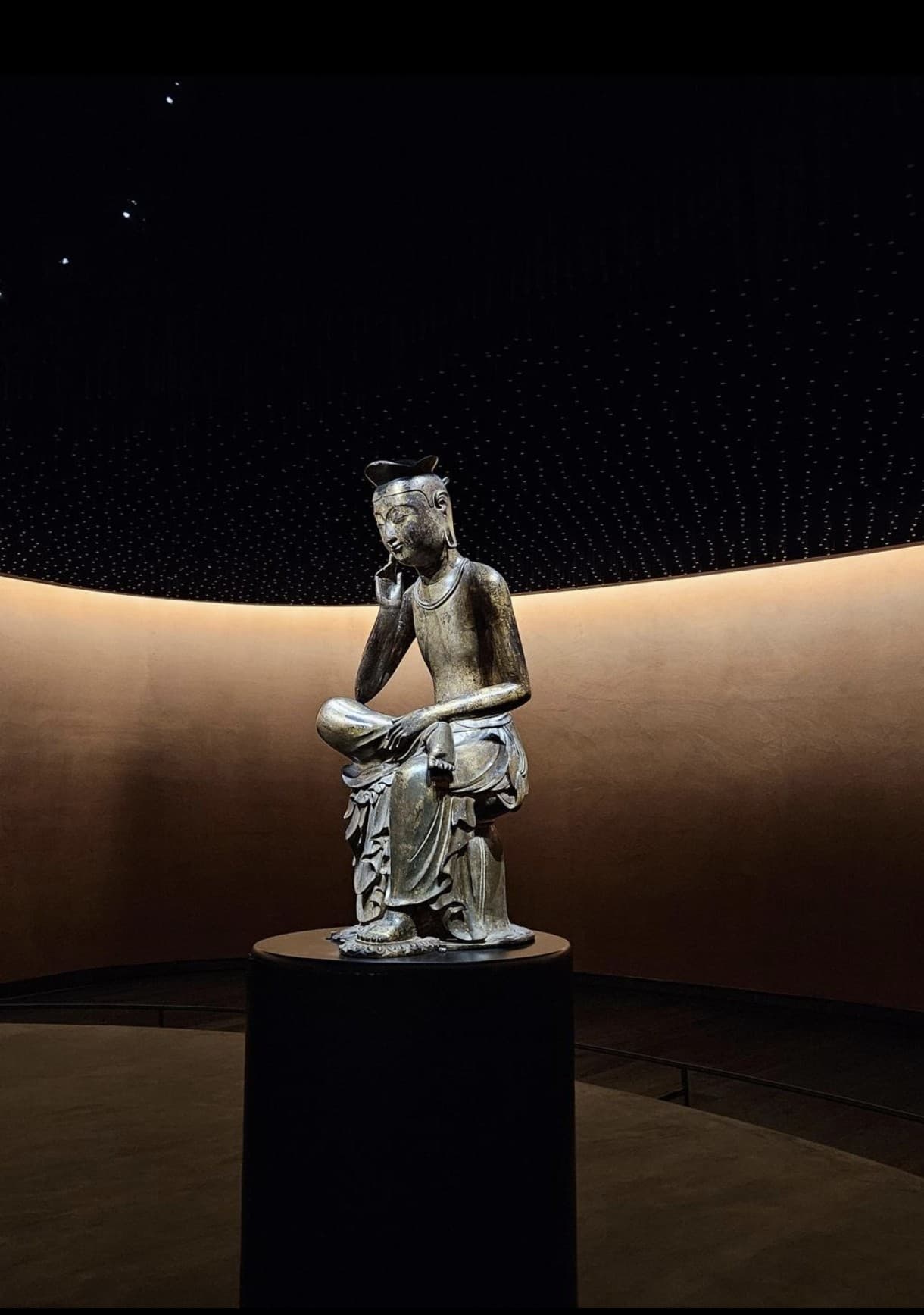 Gilt-bronze Pensive Bodhisattva statue displayed alone in the dark, starlit Room of Quiet Contemplation at the National Museum of Korea